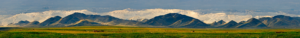 Very wide picture of mounts in the distance, beyond some green and yellow fields.